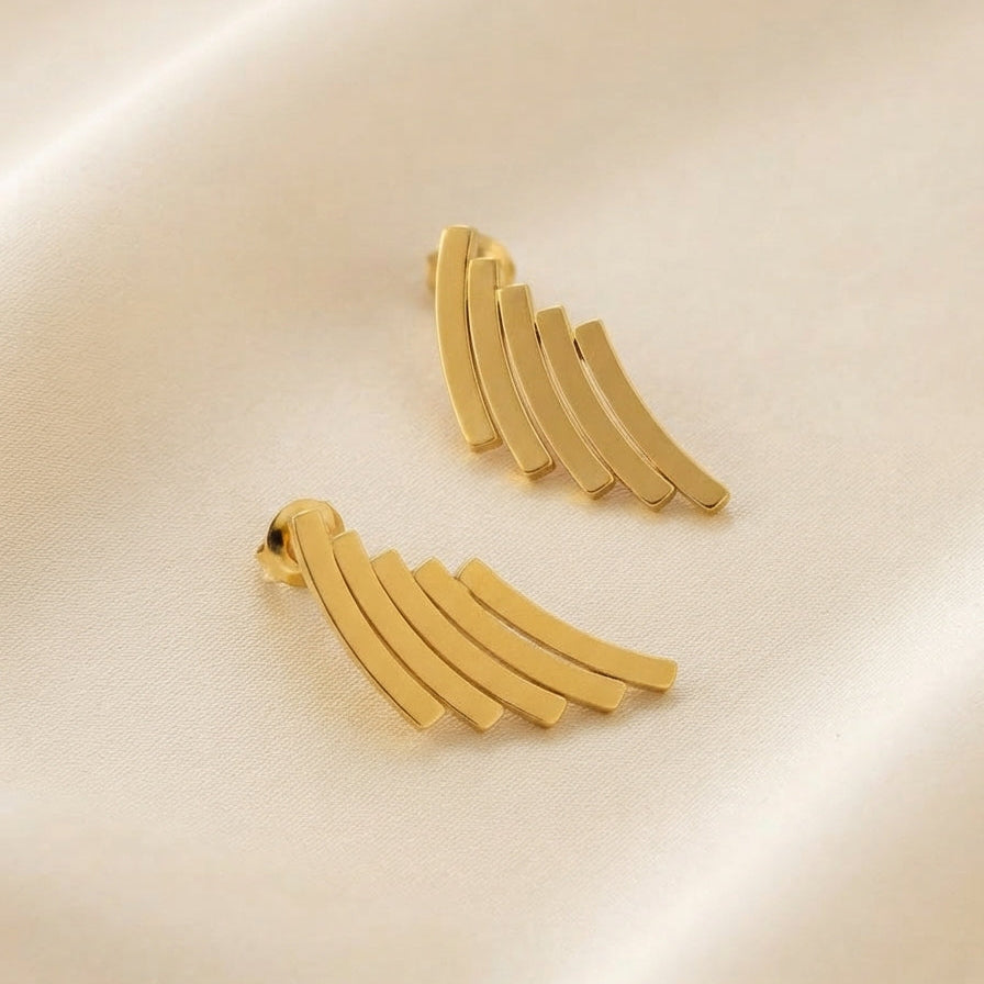 A pair of gold-toned curved bar earrings arranged on a soft cream satin fabric background.